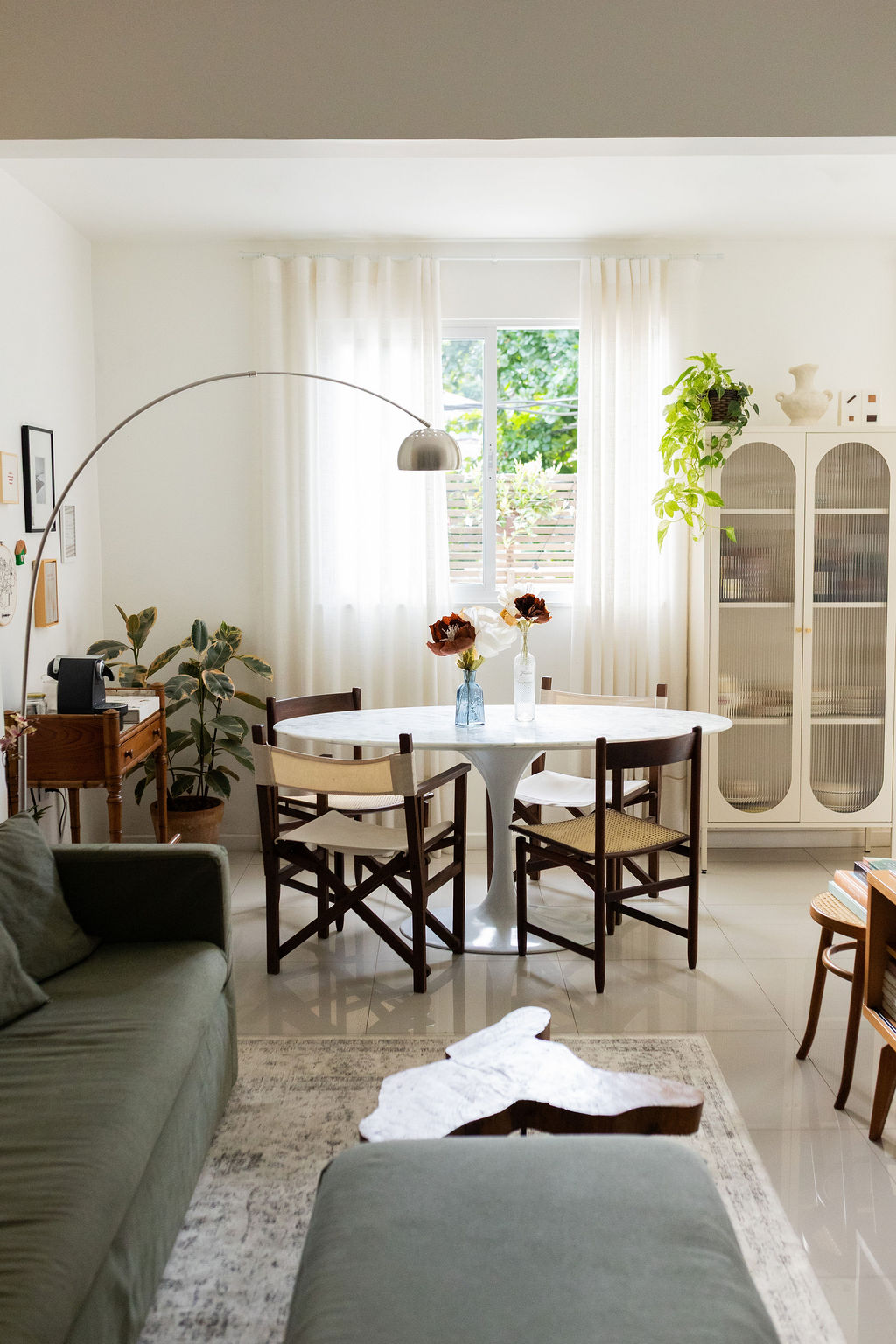 Sala de jantar com mesa oval branca, cadeiras de madeira e plantas