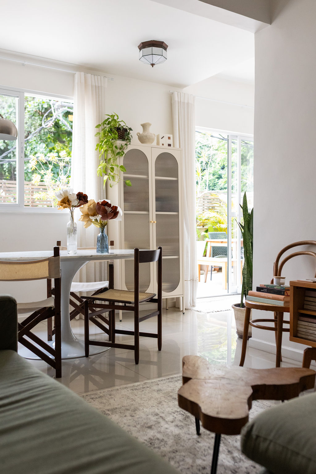 Sala de jantar iluminada com mesa branca, cristaleira e vista para o jardim