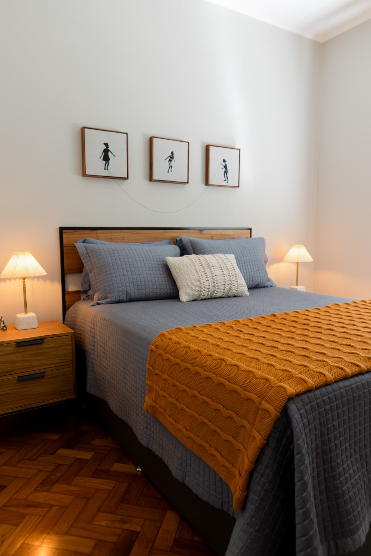 Quarto com roupa de cama cinza, manta terracota e luminárias laterais