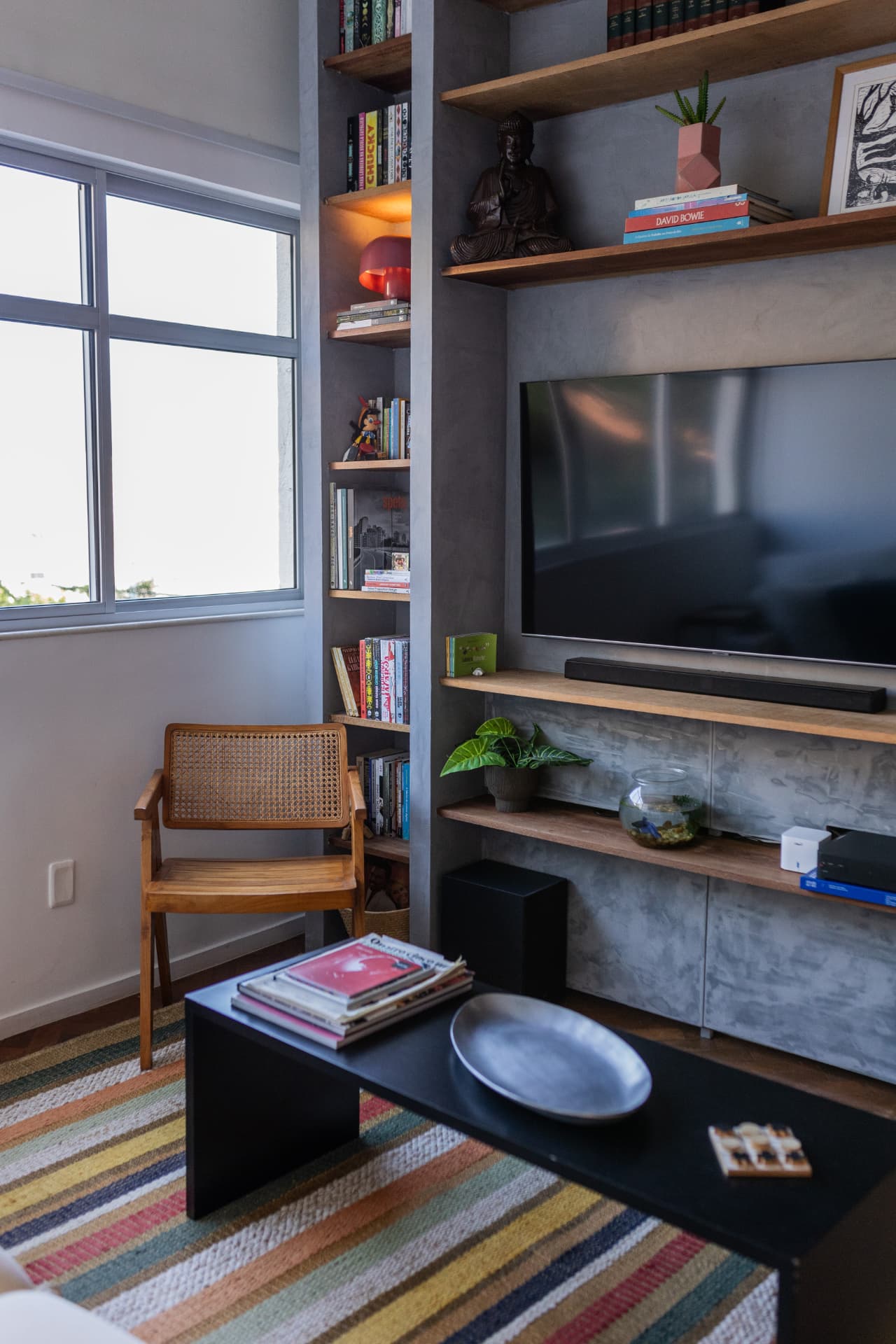 Sala de televisão com estante cinza, madeira e tapete listrado