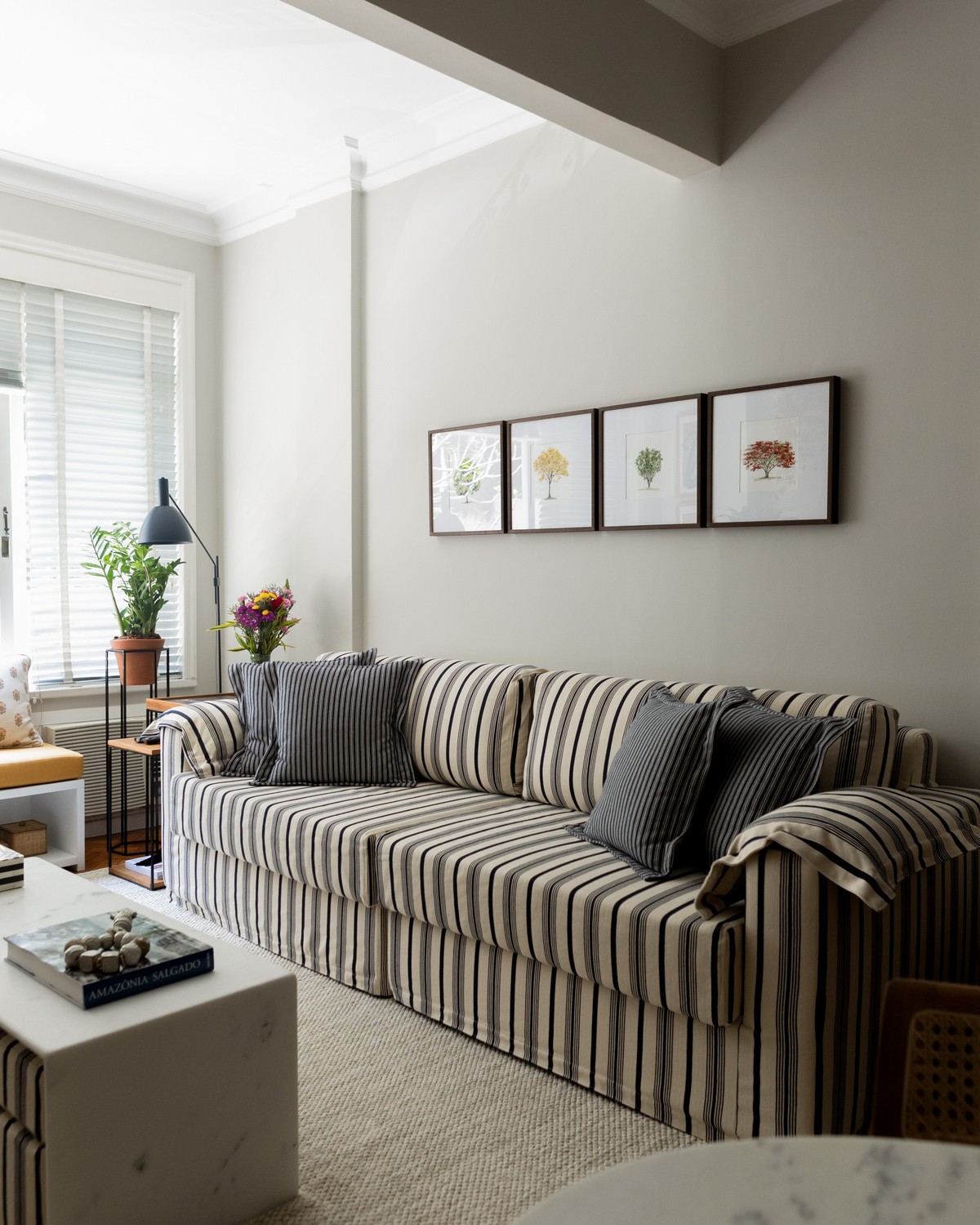 Sala com sofá listrado em preto e branco, quadros botânicos e flores