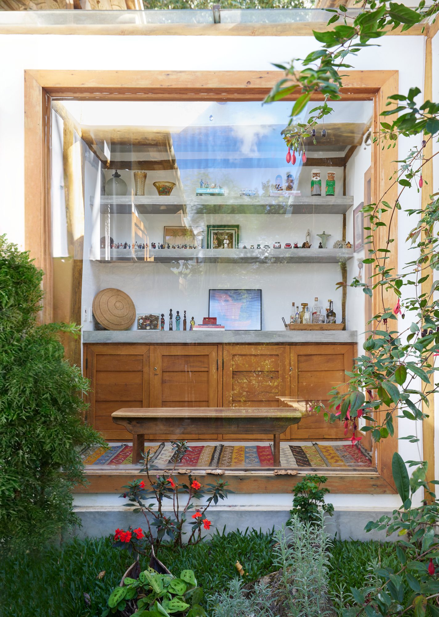 Estante da casa vista de fora pela janela, entre plantas