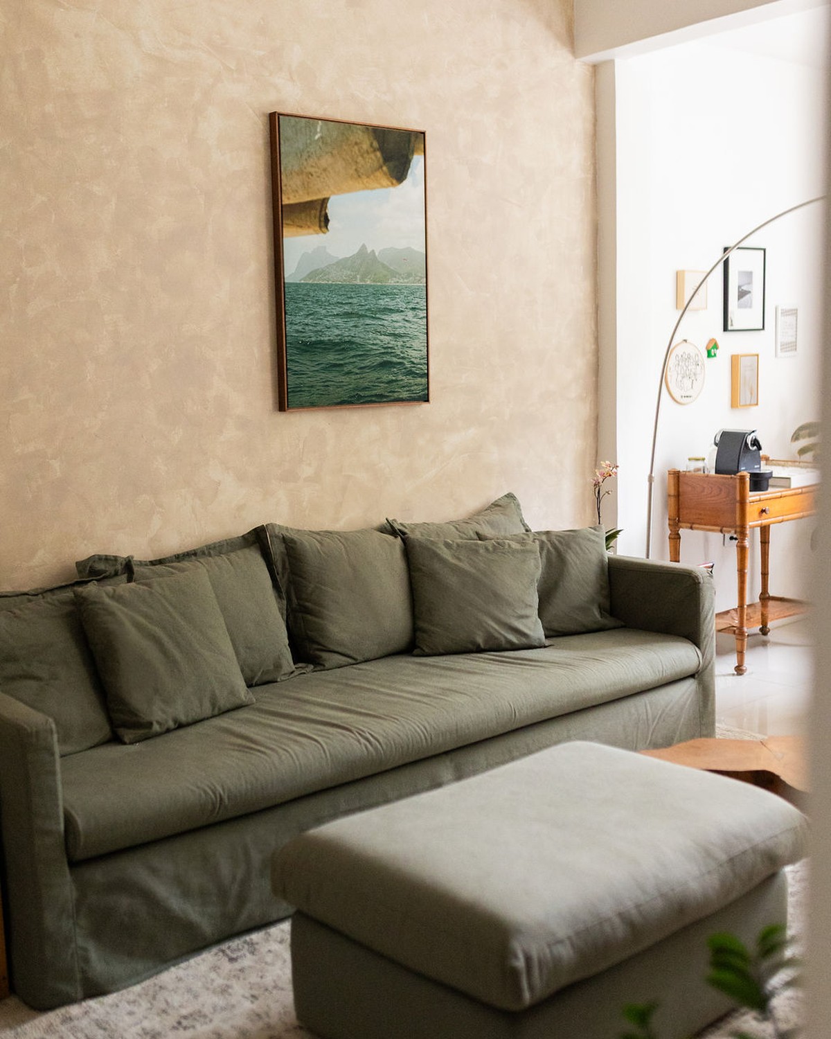 Sala com sofá verde-oliva, puff e quadro com paisagem do mar