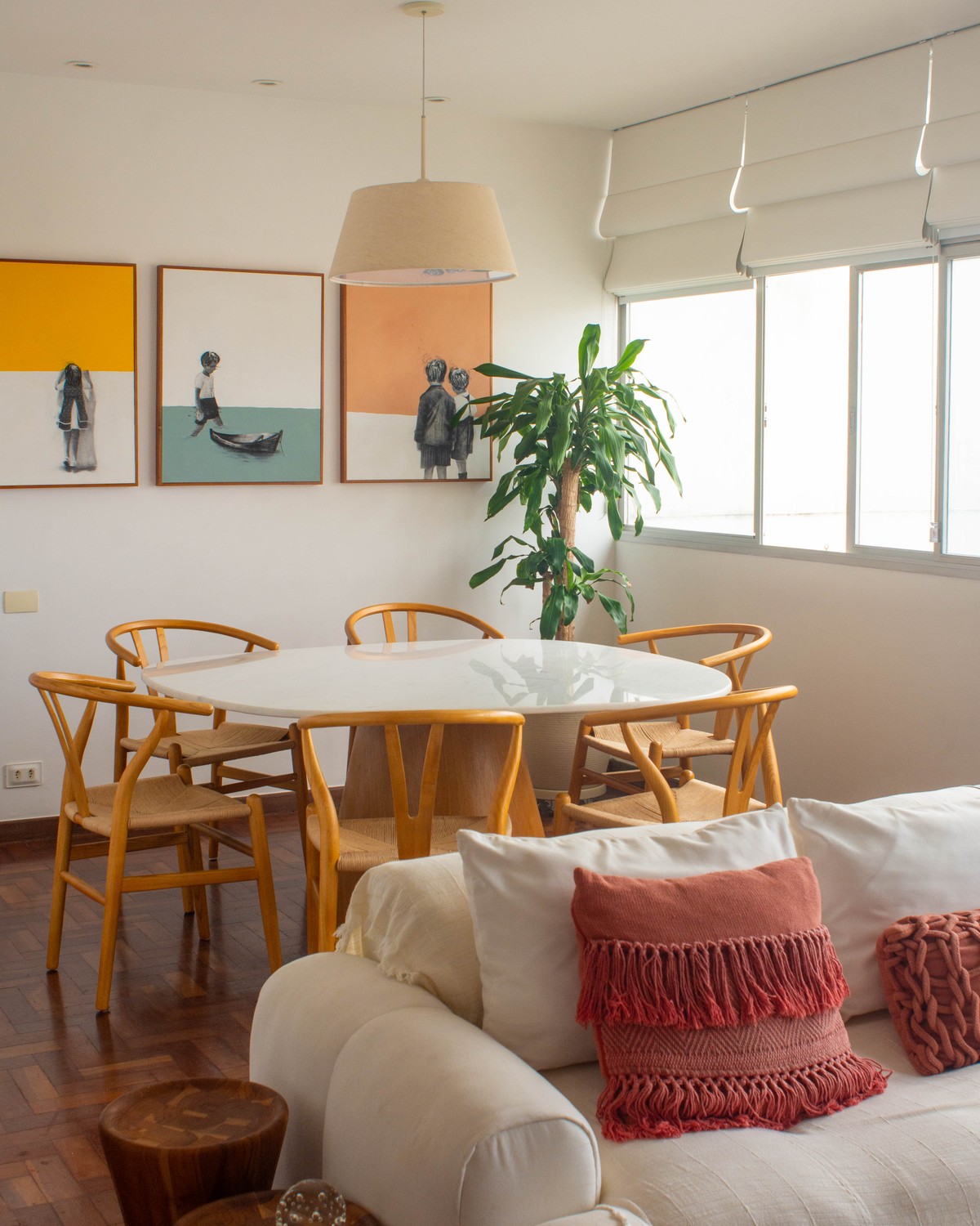 Sala de jantar com mesa redonda branca, cadeiras de madeira e tríptico de arte